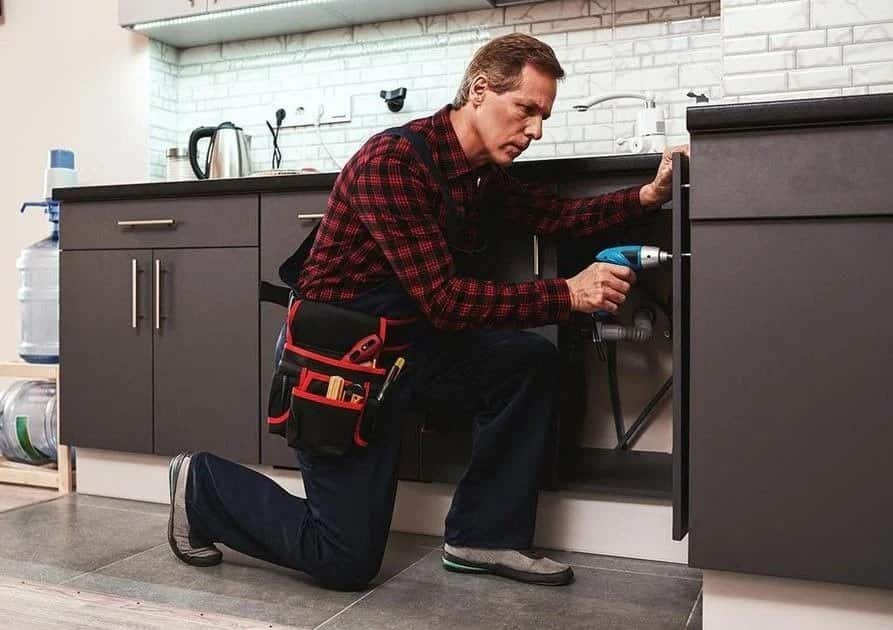 Profissional realizando reparo em pia de cozinha durante manutenção residencial